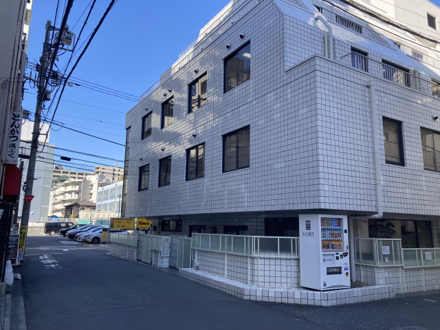 白いビルの角にあるI-DESKの看板と地下への階段